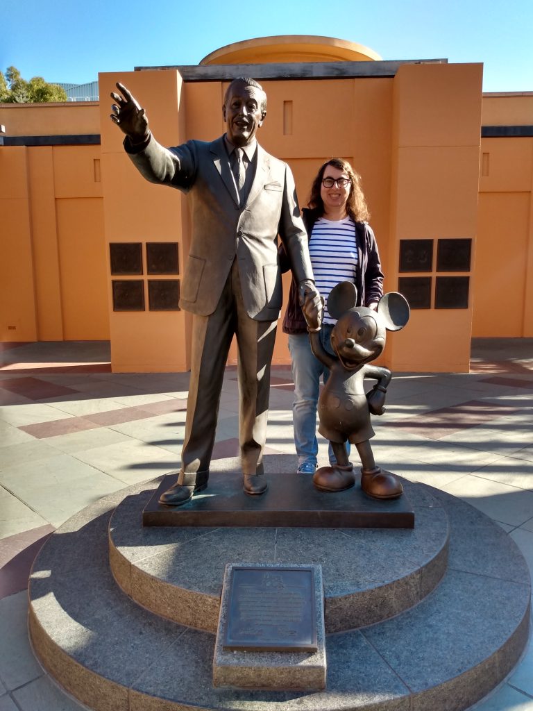 Danielle Solzman poses with statues of Walt Disney and Mickey Mouse.