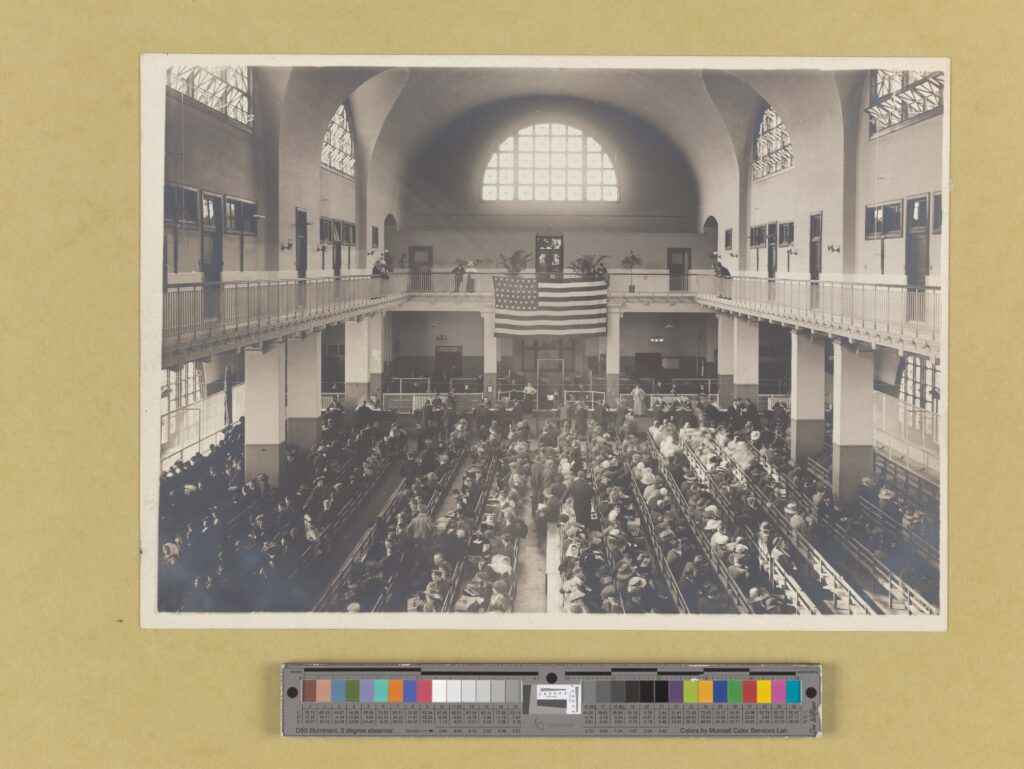 Immigrants seated on long benches at Ellis Island.