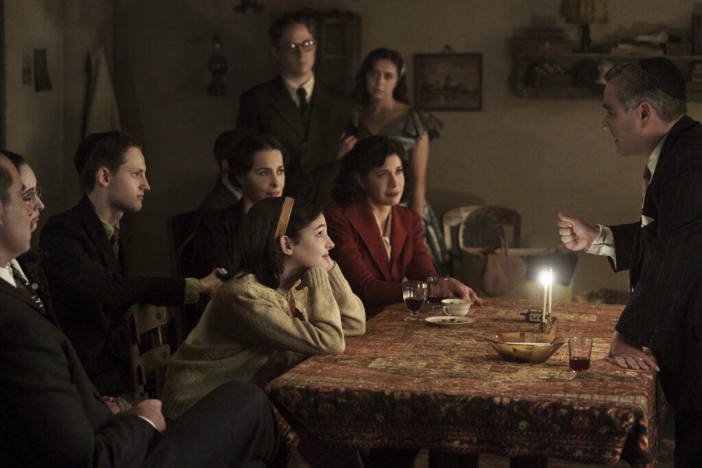 Jan and Miep Gies (Joe Cole and Bel Powley) join the Franks and the van Pels (from left: Liev Schreiber as Otto Frank, Ashley Brooke as Margot Frank, Rudi Goodman as Peter van Pels, Amira Casar as Edith Frank, Billie Boullet as Anne Frank and Caroline Catz as Mrs. van Pels) and watch as Mr. van Pels (Andy Nyman) lights the menorah during Hanukkah, as seen the upcoming limited series A SMALL LIGHT, from National Geographic and ABC Signature in partnership with Keshet Studios