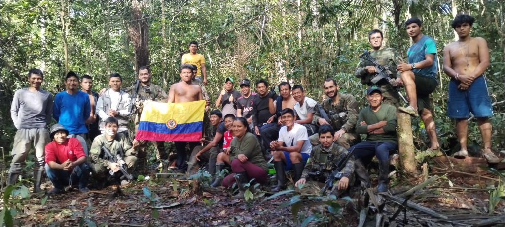 The Indigenous search team and Colombian military stand together in the jungle with the national flag.